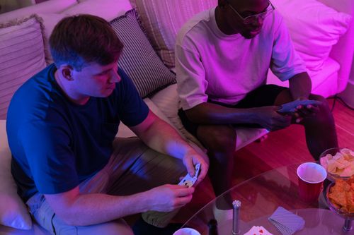Free Two friends enjoy a casual card game at home under warm pink lighting. Stock Photo