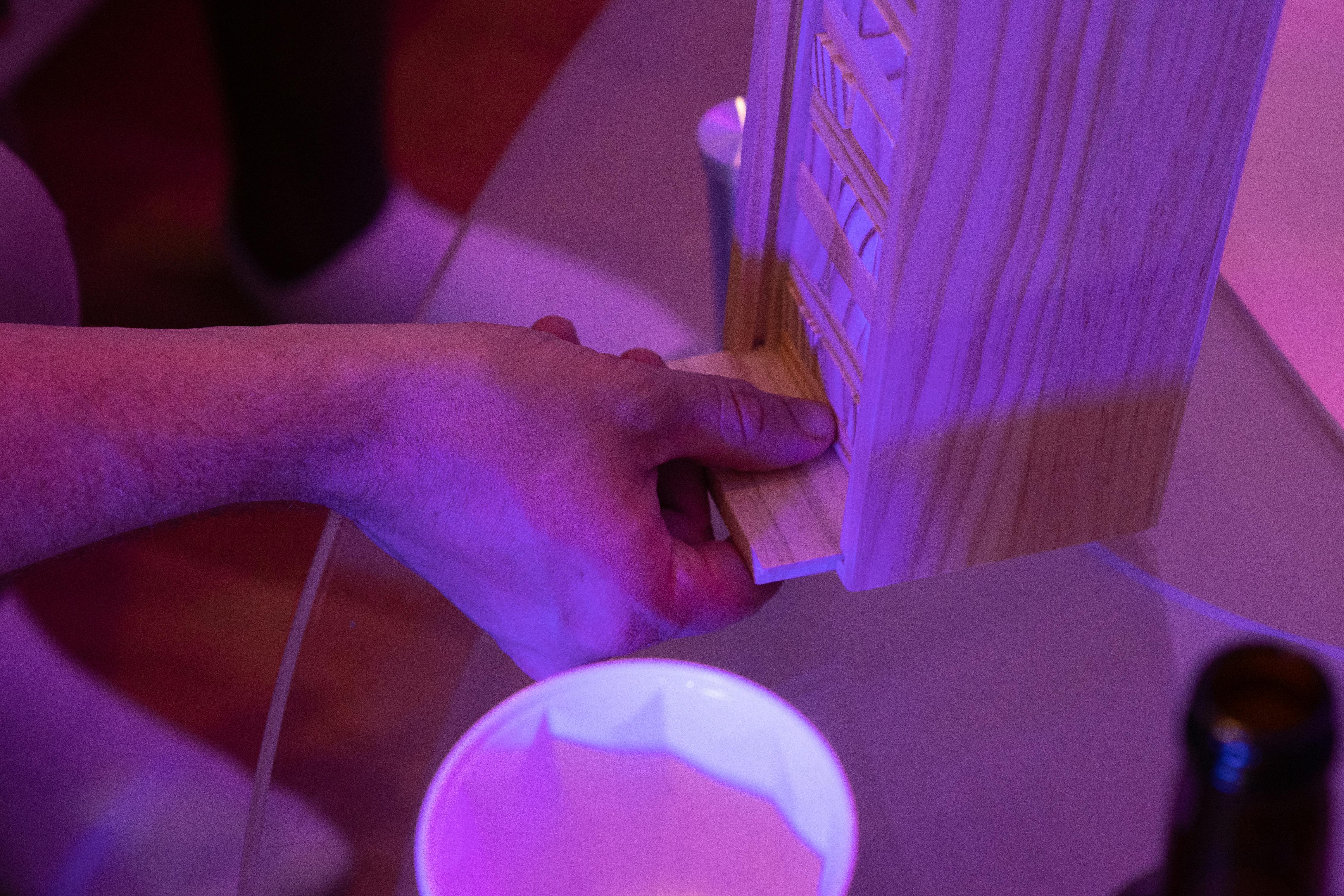 A close-up view of a hand adjusting a Jenga piece on a glass table during a party.