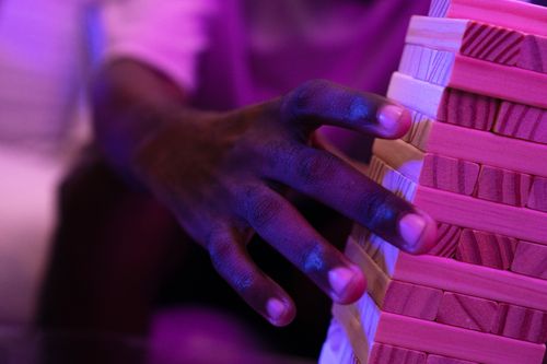 Free A hand reaches to balance a Jenga tower, illuminated by vibrant neon lighting. Stock Photo