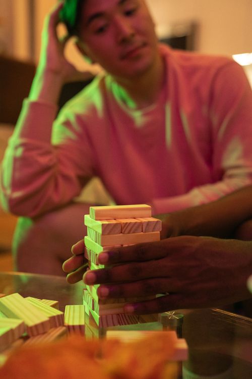 Free Close-up of friends playing Jenga at home, focusing on hand stacking wooden blocks. Stock Photo