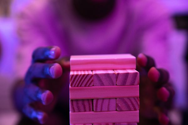 Hands stacking colorful wooden blocks under neon light