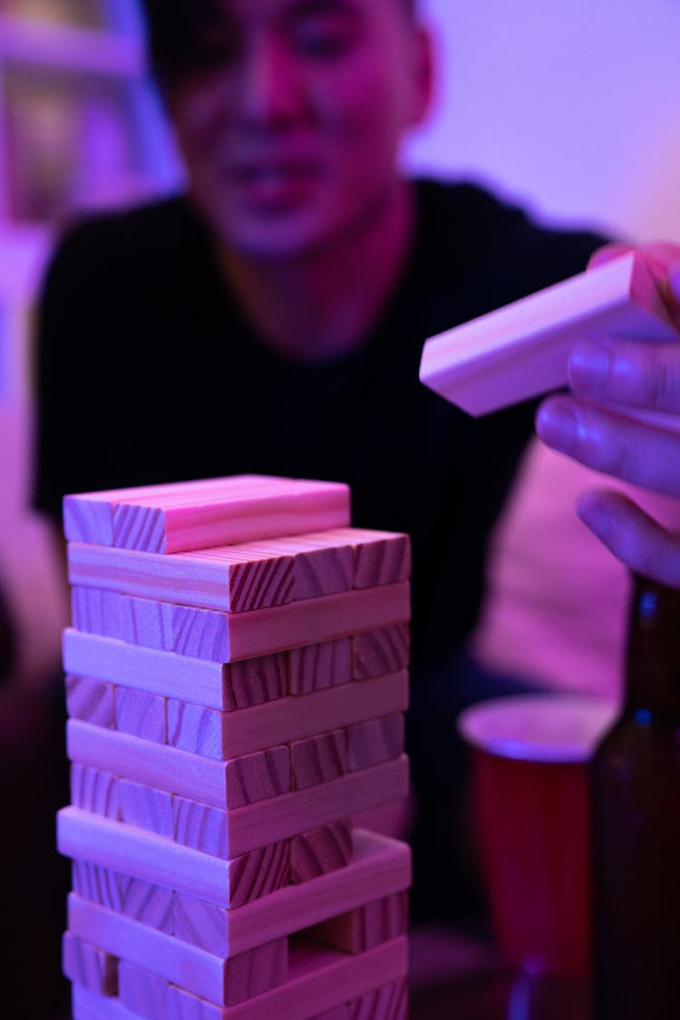 Hand Of A Person Holding A Wooden Block Over A Stack