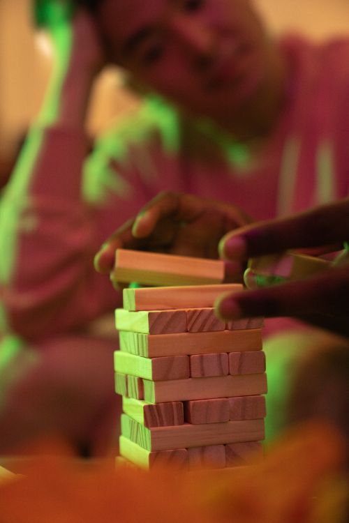Free Close-up of friends enjoying a fun Jenga game at an indoor party with warm lighting. Stock Photo