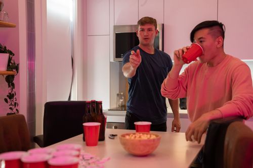 Free Two young men enjoying a game of beer pong in a modern kitchen setting. Stock Photo