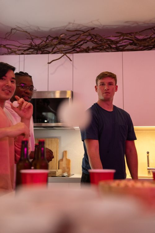 Free Group of young adults enjoying a lively beer pong game indoors with purple lighting. Stock Photo
