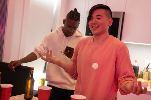 Free Two friends enjoying a game of beer pong indoors, smiling and bonding. Stock Photo