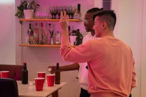 Free Two friends enjoying a game of beer pong with red cups and bottles indoors. Stock Photo