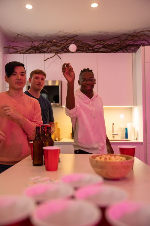 Free Three friends playing beer pong in a cozy kitchen setting, smiling and having a good time. Stock Photo