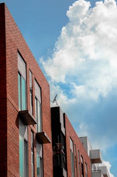 Low-angle view of a modern apartment building against a bright blue sky with clouds.