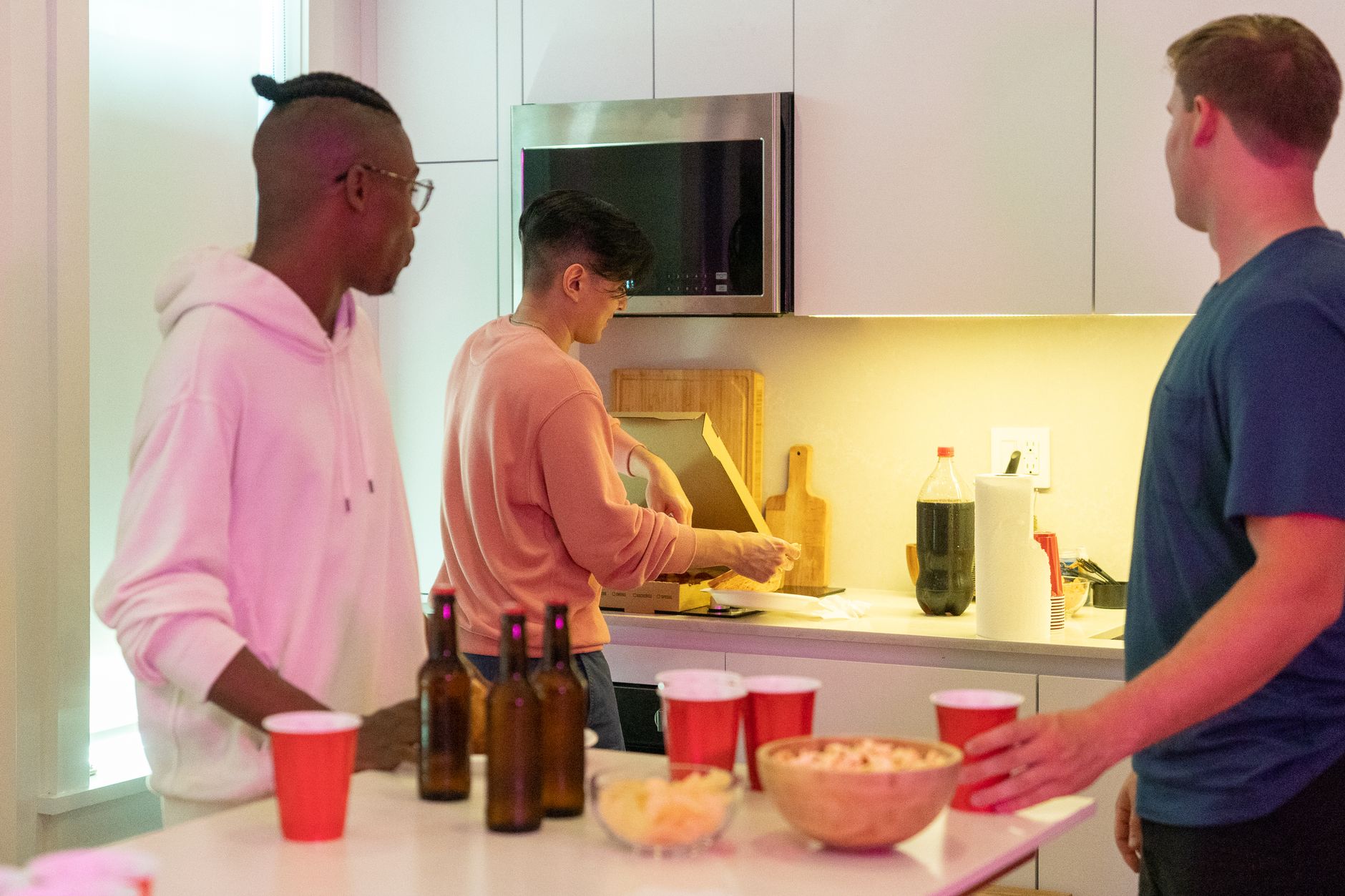 Três jovens na cozinha de um apartamento organizando compras de mercado sobre a bancada.