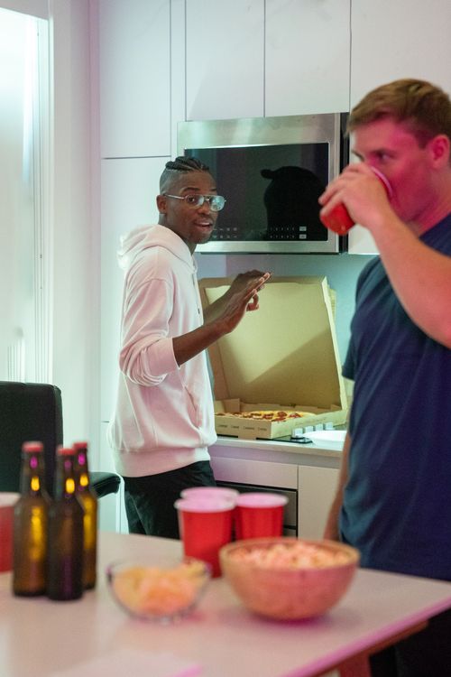 Free Two men enjoying pizza and drinks indoors at a casual party setting. Stock Photo