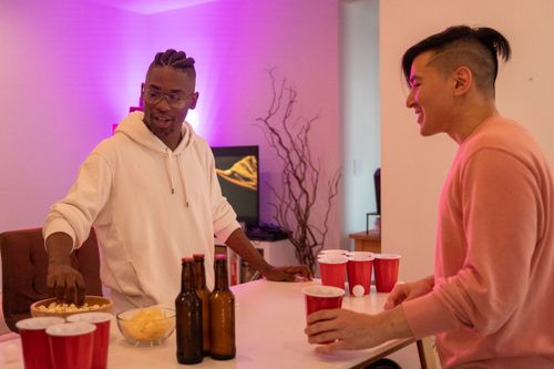 Free Two friends playing beer pong with snacks and beer on a casual night indoors. Stock Photo