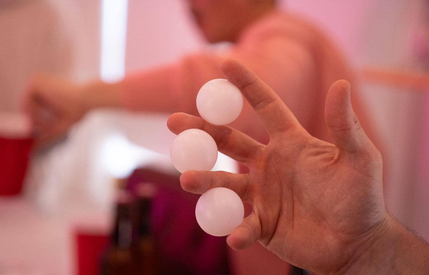 A close-up shot of a hand holding three white ping pong balls indoors.