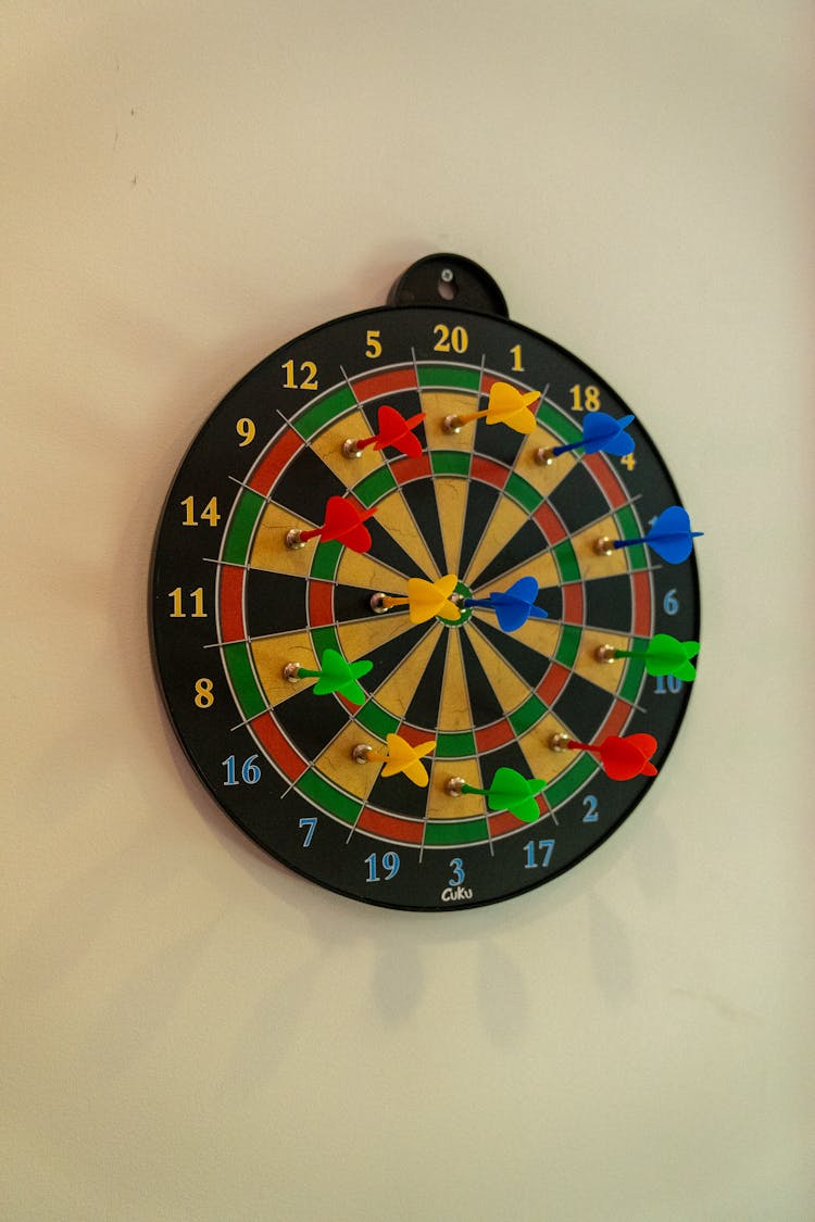 A Dartboard On The Wall With Colorful Darts 