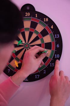 Person playing darts, adjusting hit darts on dartboard, focusing on leisure activity.