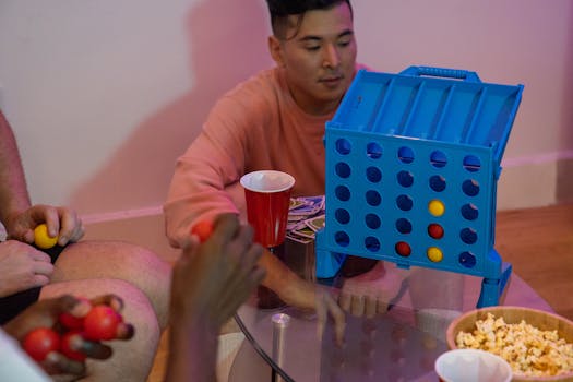 Group of friends enjoying Connect Four with snacks and drinks indoors.