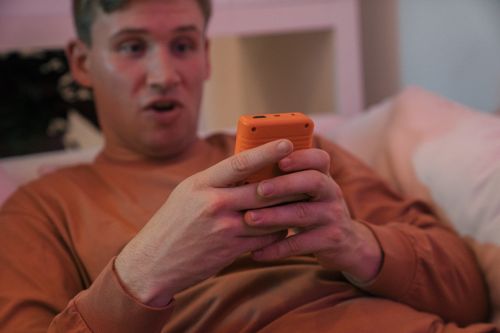 Free A man lying in bed looking surprised while using a smartphone indoors. Stock Photo