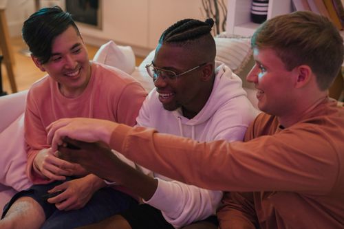 Free Three male friends enjoy time together indoors, sharing laughter and camaraderie, showcasing diversity. Stock Photo