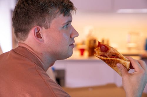 Close-Up Shot of a Man Holding a Slice of Pizza