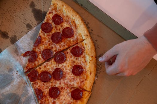 Hand reaching for a delicious pepperoni pizza slice in a cardboard box.