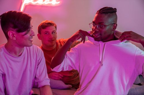 Free Three friends enjoying a casual evening indoors with pink neon lighting, capturing smiles and lively conversation. Stock Photo