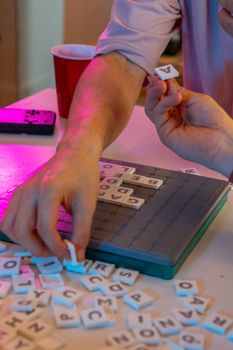 Close-up of friends playing a word board game, showcasing hands and tiles.