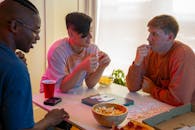 Man in Pink Crew Neck T-shirt Sitting Beside Woman in Orange Long Sleeve Shirt Eating