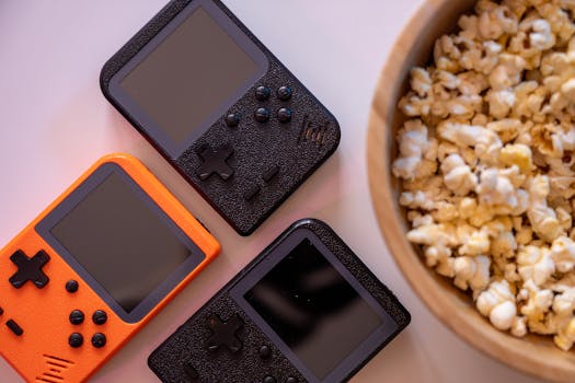 Close-up of retro handheld game consoles and popcorn, perfect for gaming nights.