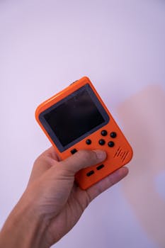 Close-up of a retro orange gaming console held in a hand, showcasing buttons and screen.