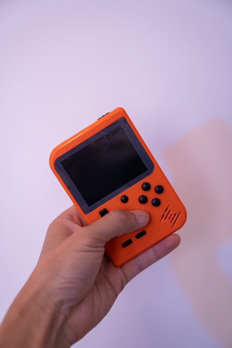 A Person Holding An Orange Game Boy