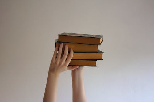 Person Holding A Stack of Hardbound Books