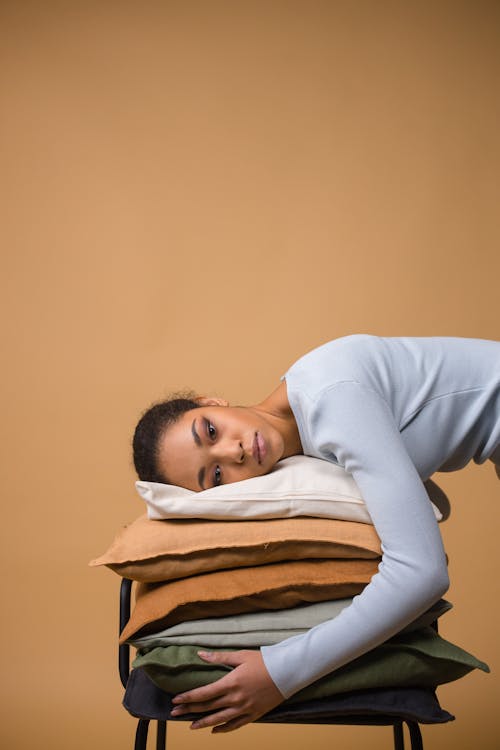 A Woman in White Long Sleeves Lying Her Head on the Stack of Pillows
