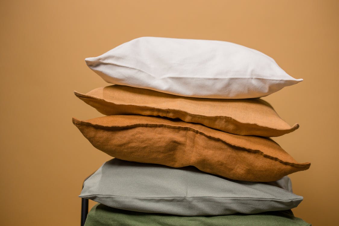 Stack of different colorful pillows folded and placed in stack on chair isolated on dark beige background