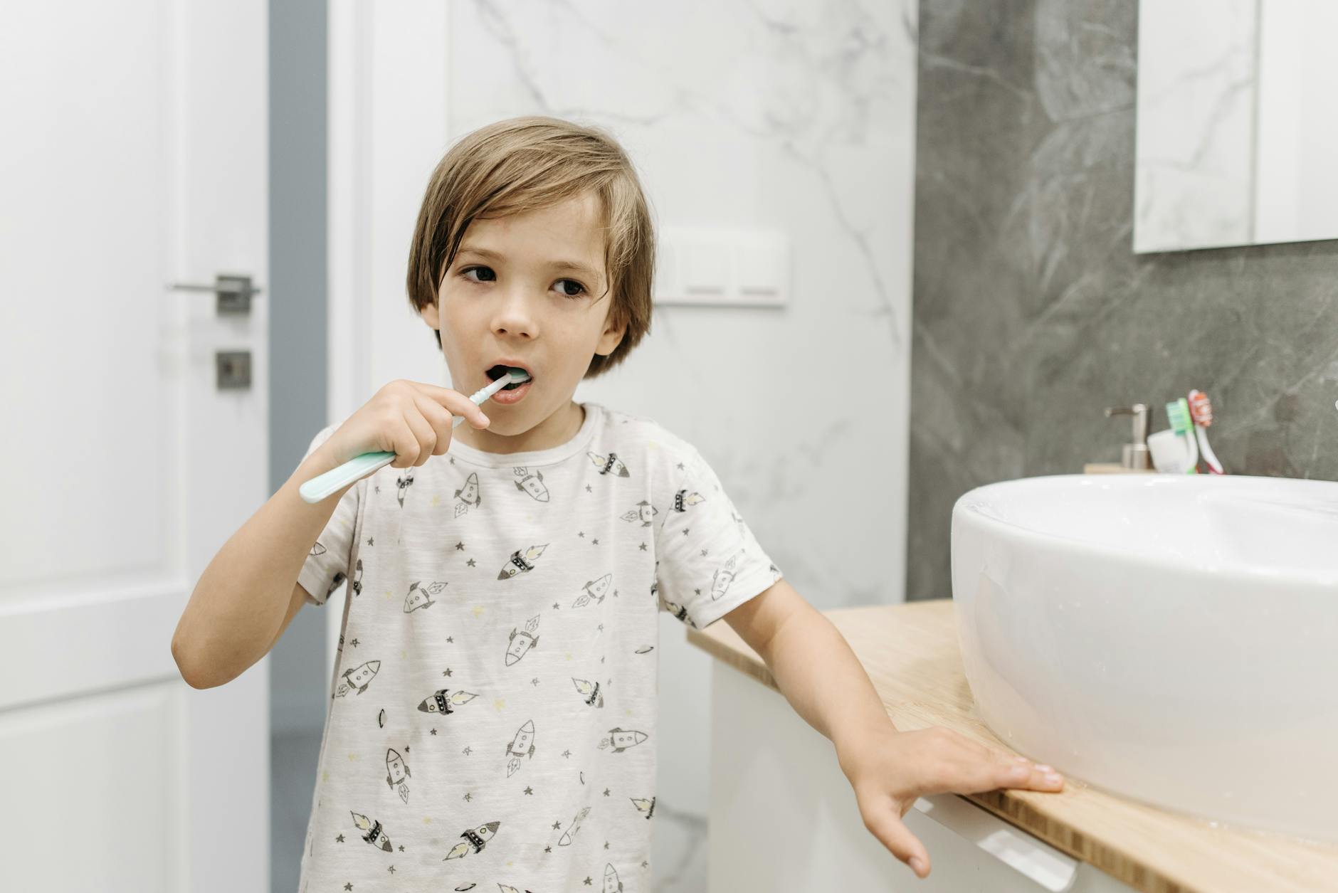 A young blond boy practicing dental hygiene by brushing his teeth indoors.