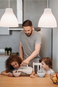 Father pouring milk for kids during breakfast in a cozy kitchen setting.