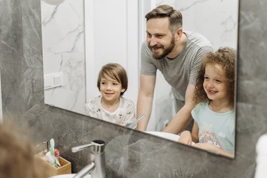 A father and his children smiling at their reflection in a bathroom mirror.