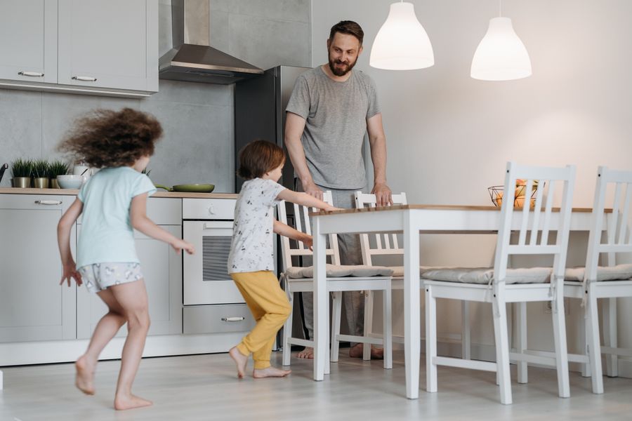 Father and kids playing joyfully in a spacious, bright kitchen.