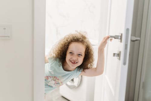 A Young Girl Smiling while Holding a Door Handle