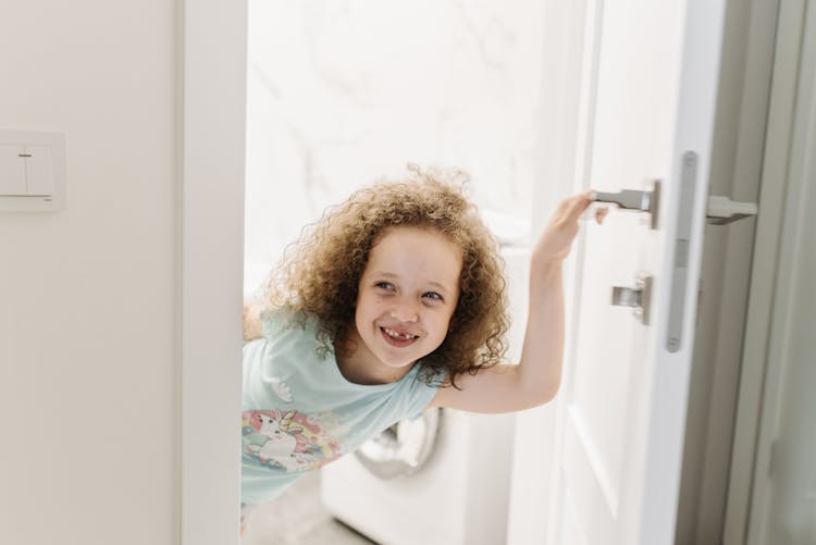 A Young Girl Smiling While Holding A Door Handle