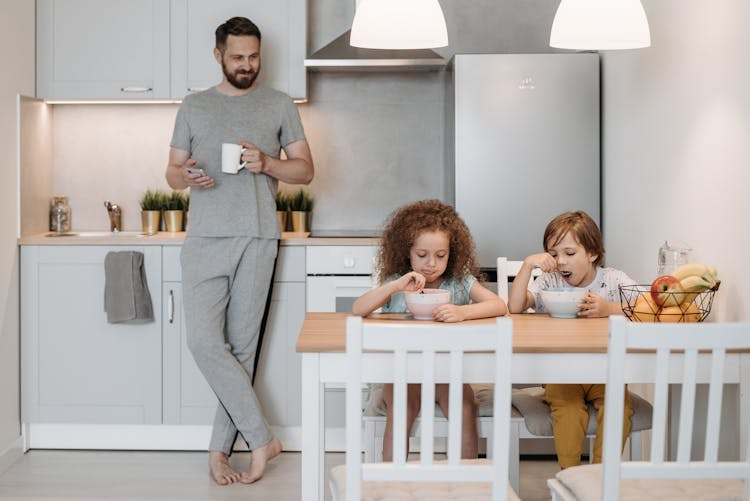 A Man Looking At His Kids While Eating Breakfast