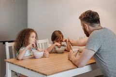 A father and his children having breakfast together at a wooden table indoors, promoting family bonding.