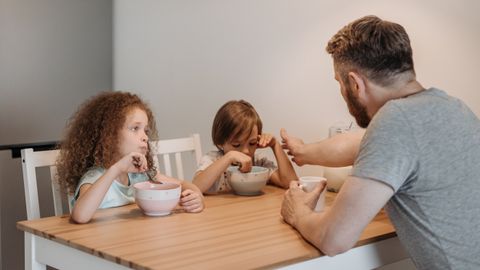 A father and his children having breakfast together at a wooden table indoors, promoting family bonding.