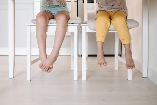 Two children sitting on chairs indoors, feet dangling playfully.
