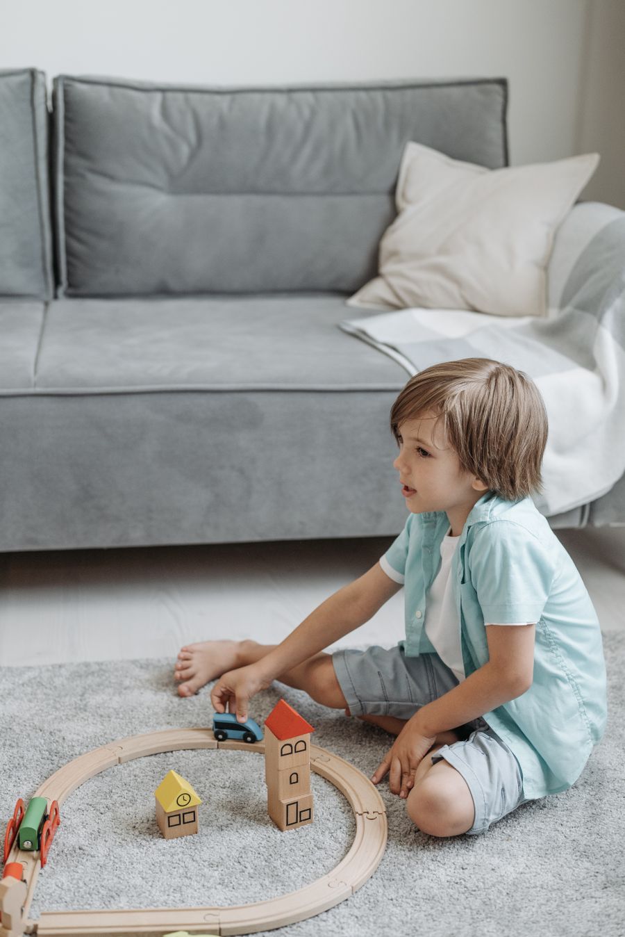 Young boy playing with wooden toy trains on the floor of a living room