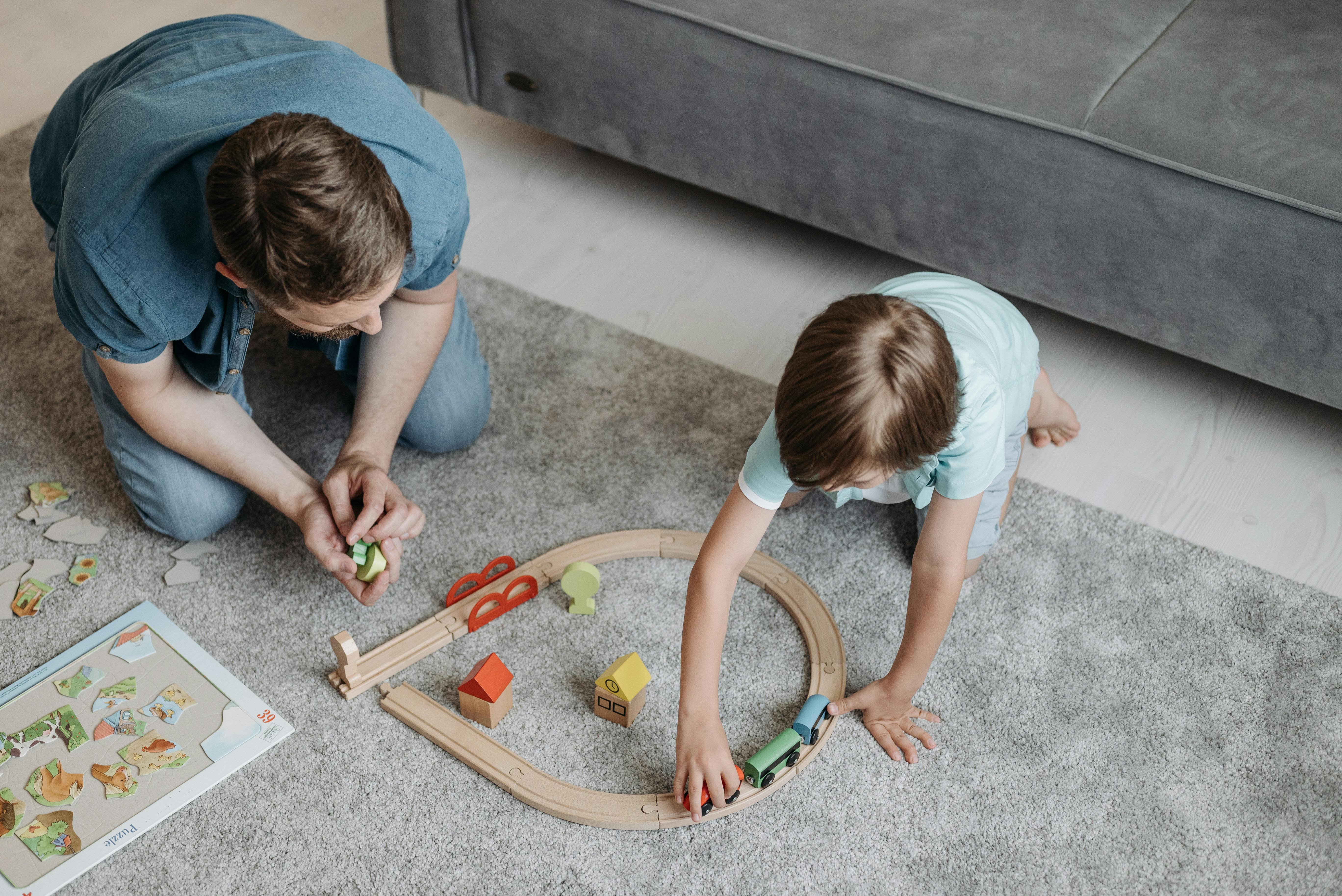 Father and son enjoy bonding time playing with a wooden train set on a cozy carpet indoors.