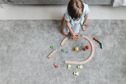 Free A child playing with a colorful toy train set on a living room carpet. Stock Photo