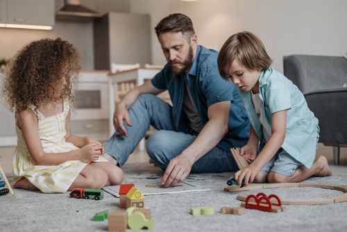 Free Father playing with his son and daughter in a cozy living room setting, engaging with toys on the carpet. Stock Photo