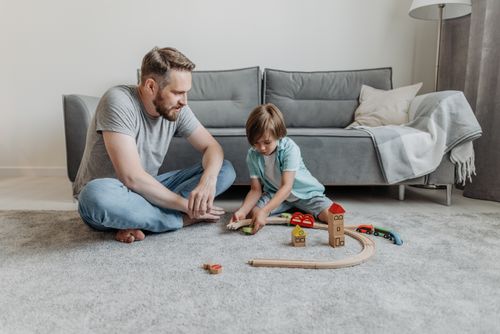Free Father and son enjoying quality time playing with a wooden toy train set on the living room floor. Stock Photo
