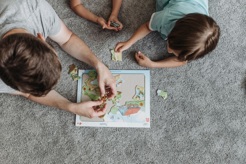 Father and children enjoying puzzle time together on a cozy carpeted floor.