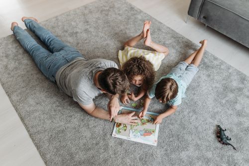 Free Father and kids enjoy quality time solving a puzzle together on a living room rug. Stock Photo